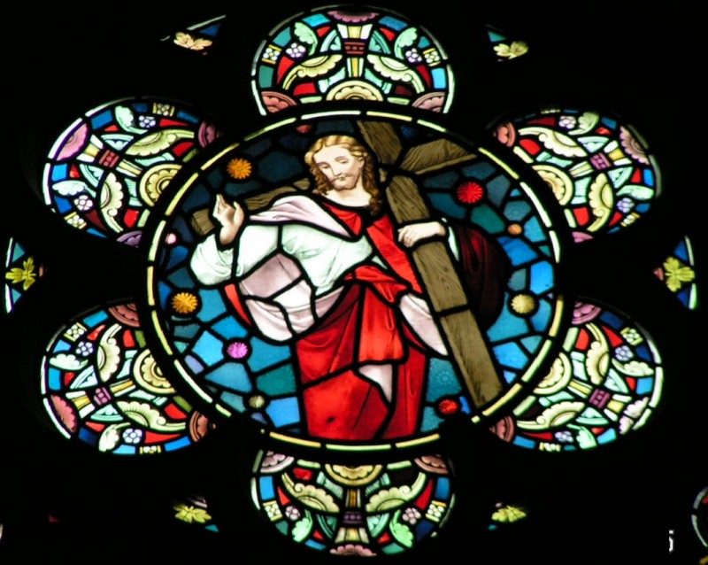 Jesus, dressed in red and white robes, is shown carrying a cross